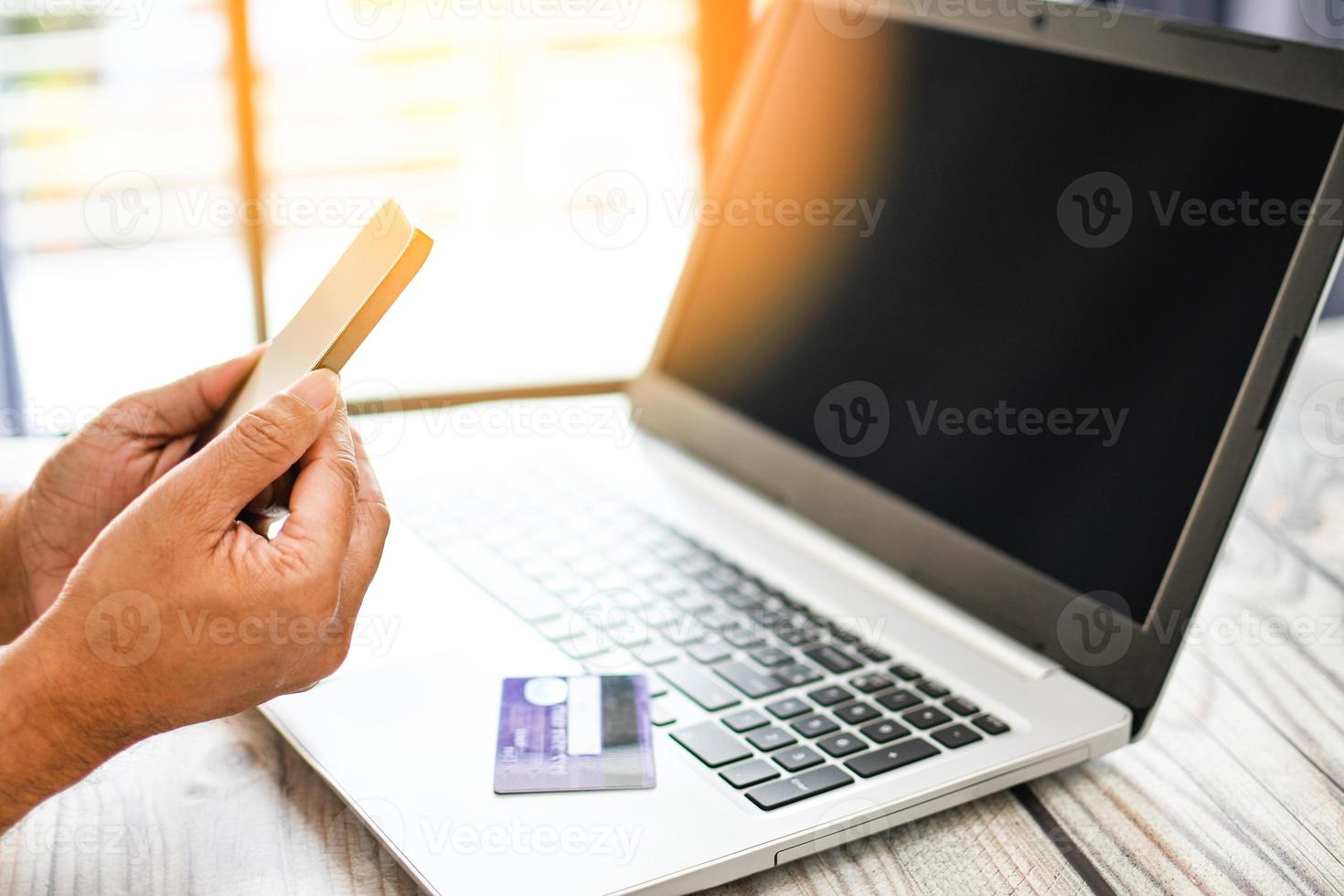 la mano de un hombre sostiene un teléfono inteligente para comprar en línea. los empresarios transfieren dinero con una aplicación móvil. una tarjeta de crédito o débito colocada en una computadora portátil. de cerca. enfoque selectivo. fondo borroso foto