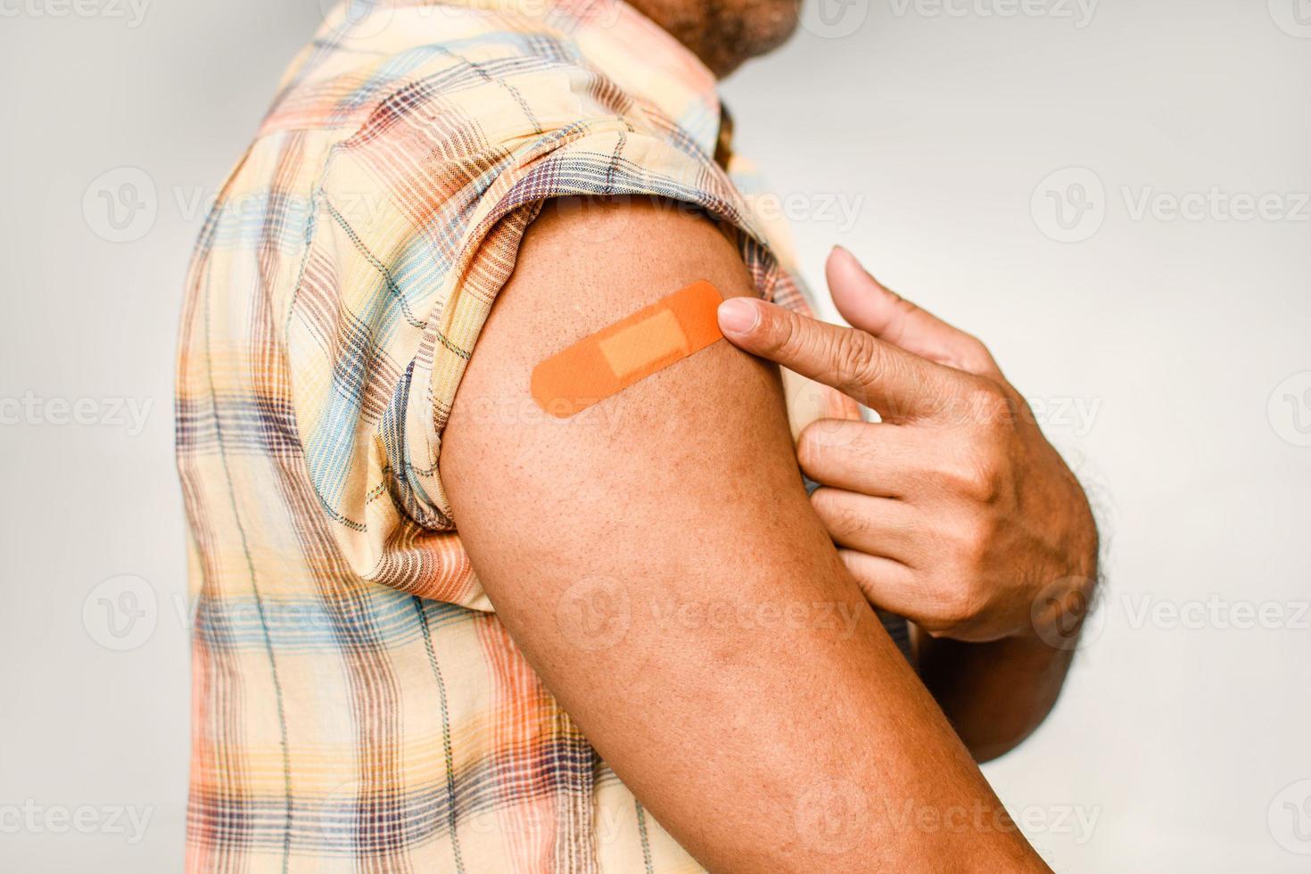 An orange plaster is attached to the man's arm. Concept for first aid after coronavirus COVID-19 vaccination, and professional, medical, needle, blood, cancer. Closeup, white blurred background photo