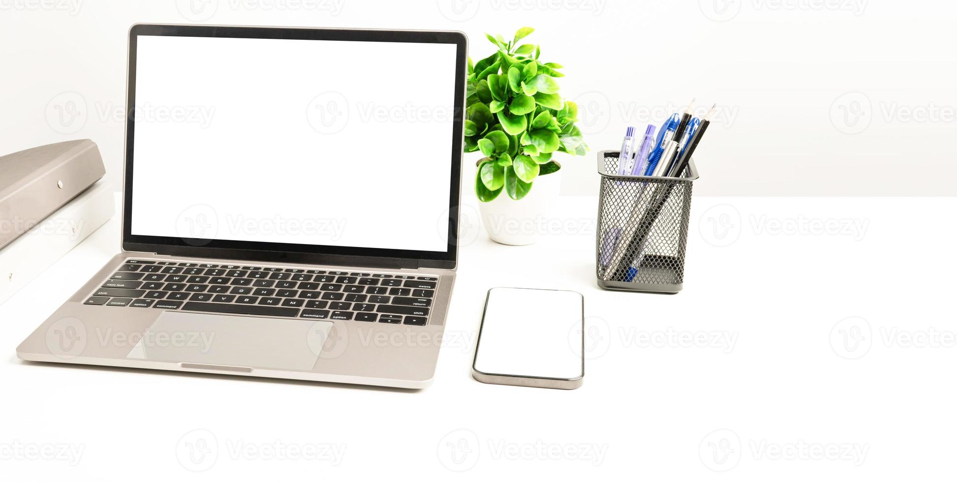 una computadora portátil de pantalla blanca en blanco sobre una mesa blanca en la oficina. teléfono inteligente de pantalla blanca en blanco. concepto de trabajo usando tecnología. copie el espacio a la derecha para el diseño o el texto, el primer plano, el gris y el fondo borroso foto