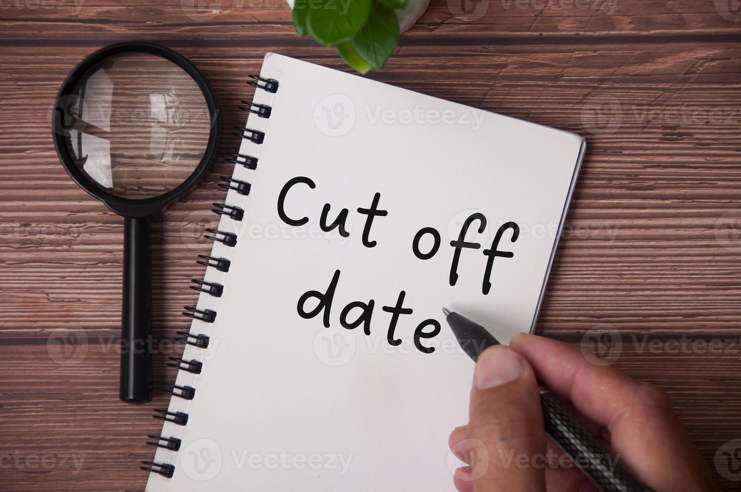 Hand writing cut of date on notepad with table plant and magnifying glass on wooden table. photo