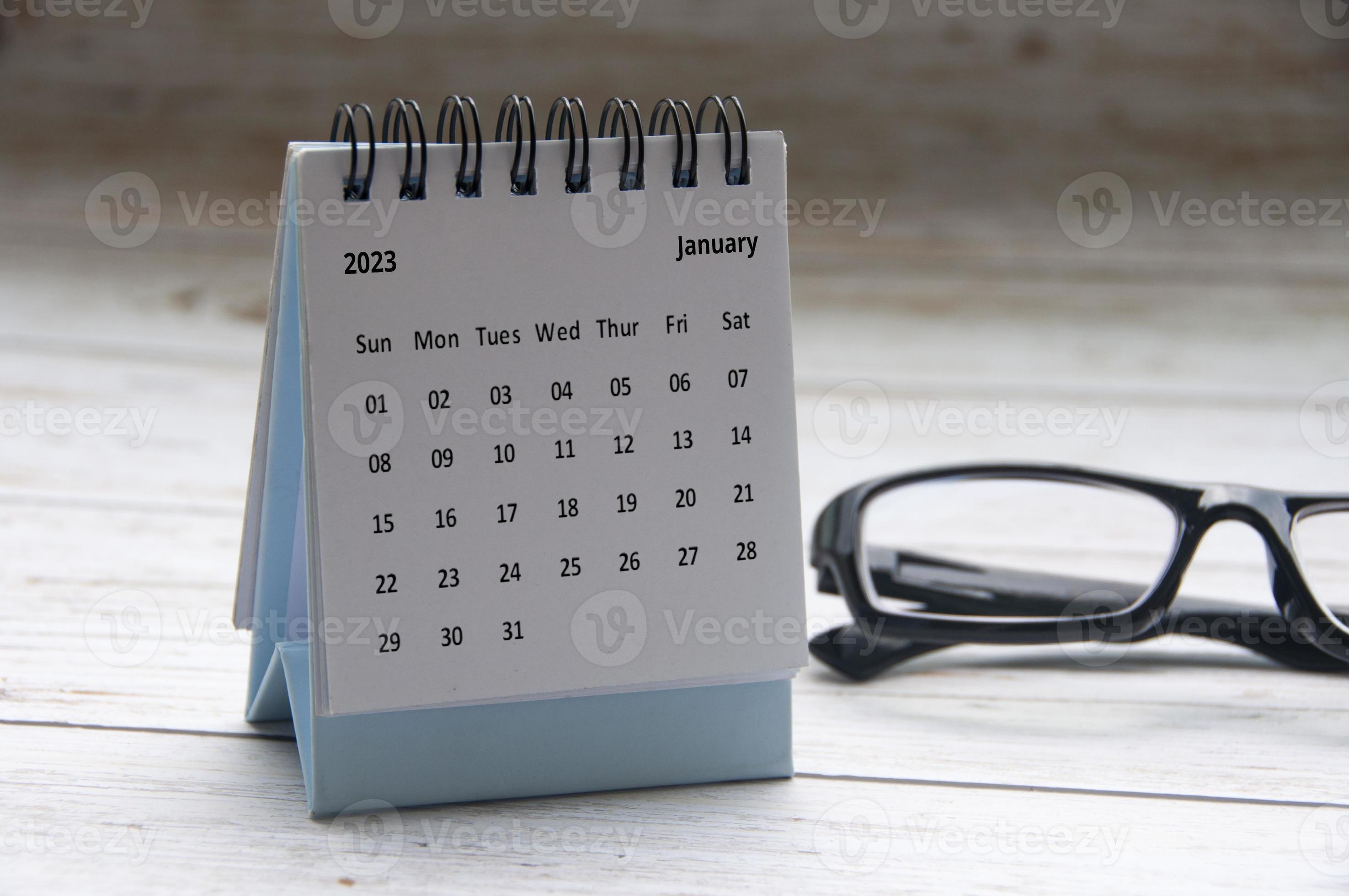 January 2023 white desk calendar with glasses on wooden table