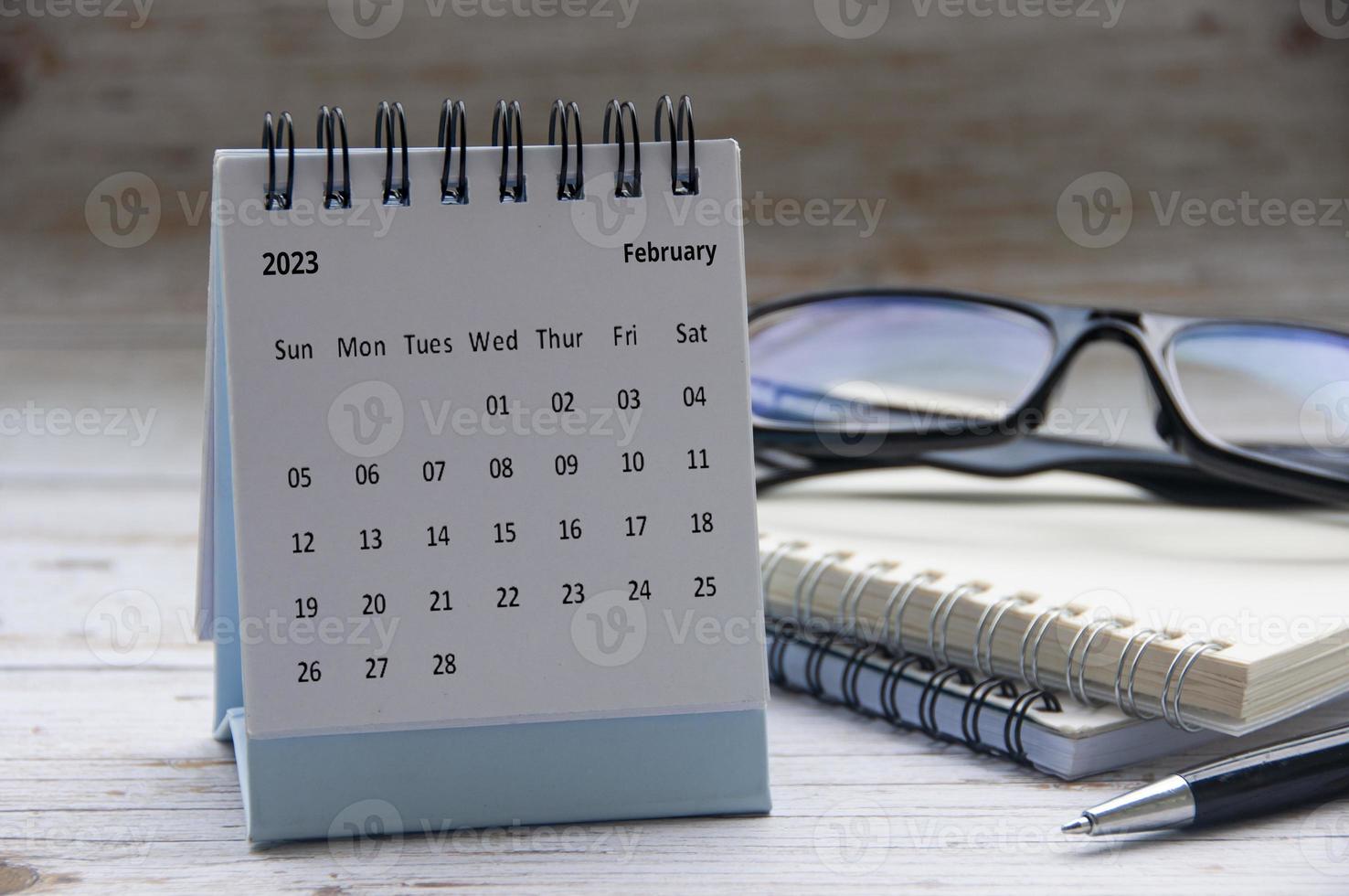 February 2023 white desk calendar with notepad and glasses background. New year and month concept. photo