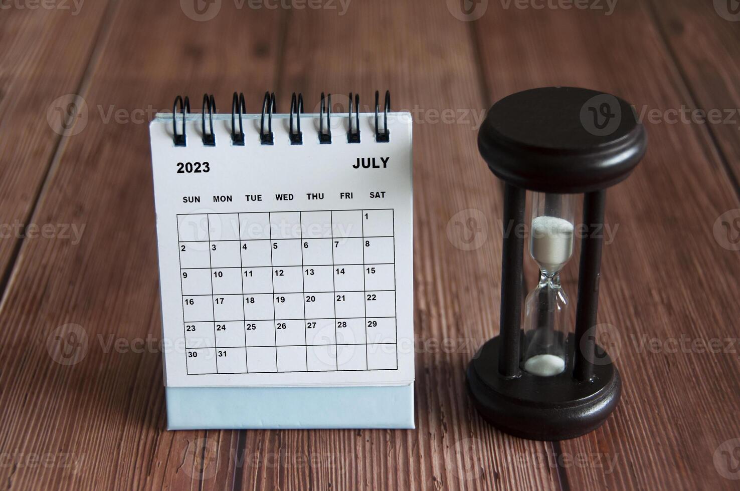 July 2023 white desk calendar with minute glass on wooden table. photo