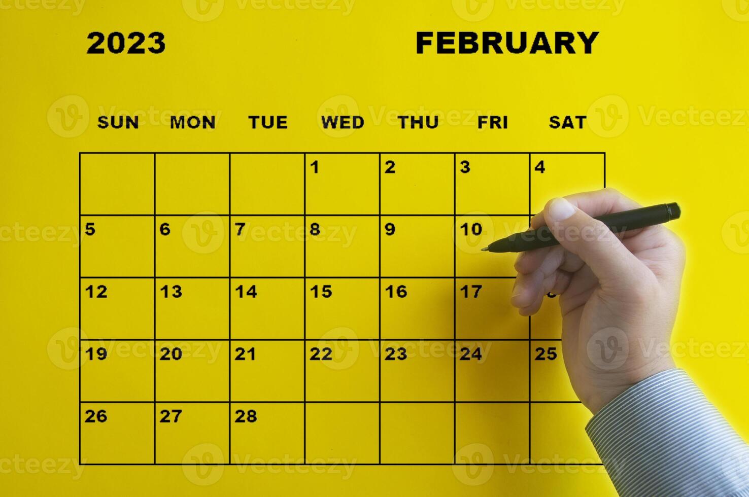 calendario de febrero de 2023 con mano sosteniendo un bolígrafo negro sobre fondo amarillo. foto