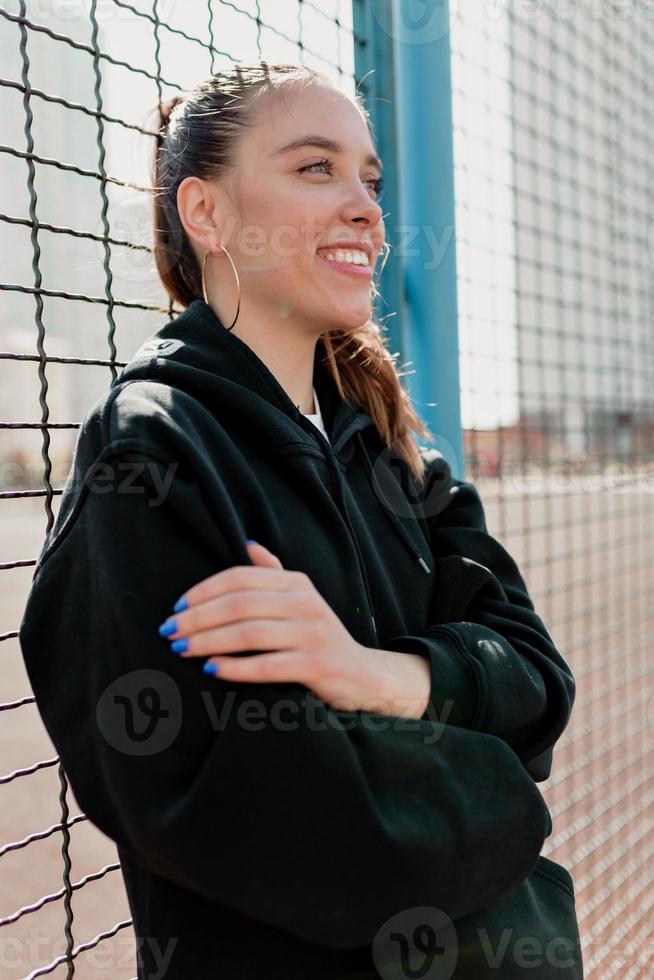 mujer positiva con peinado oscuro vistiendo ropa oscura sonriendo y divirtiéndose en la ciudad en un día cálido y soleado foto