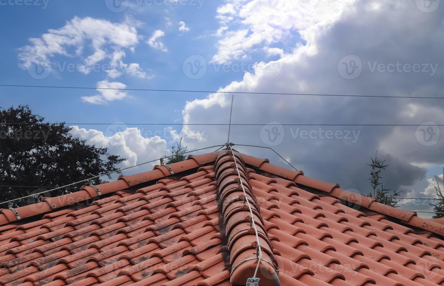 A roof with red shingles and a lightning conductor on it. photo