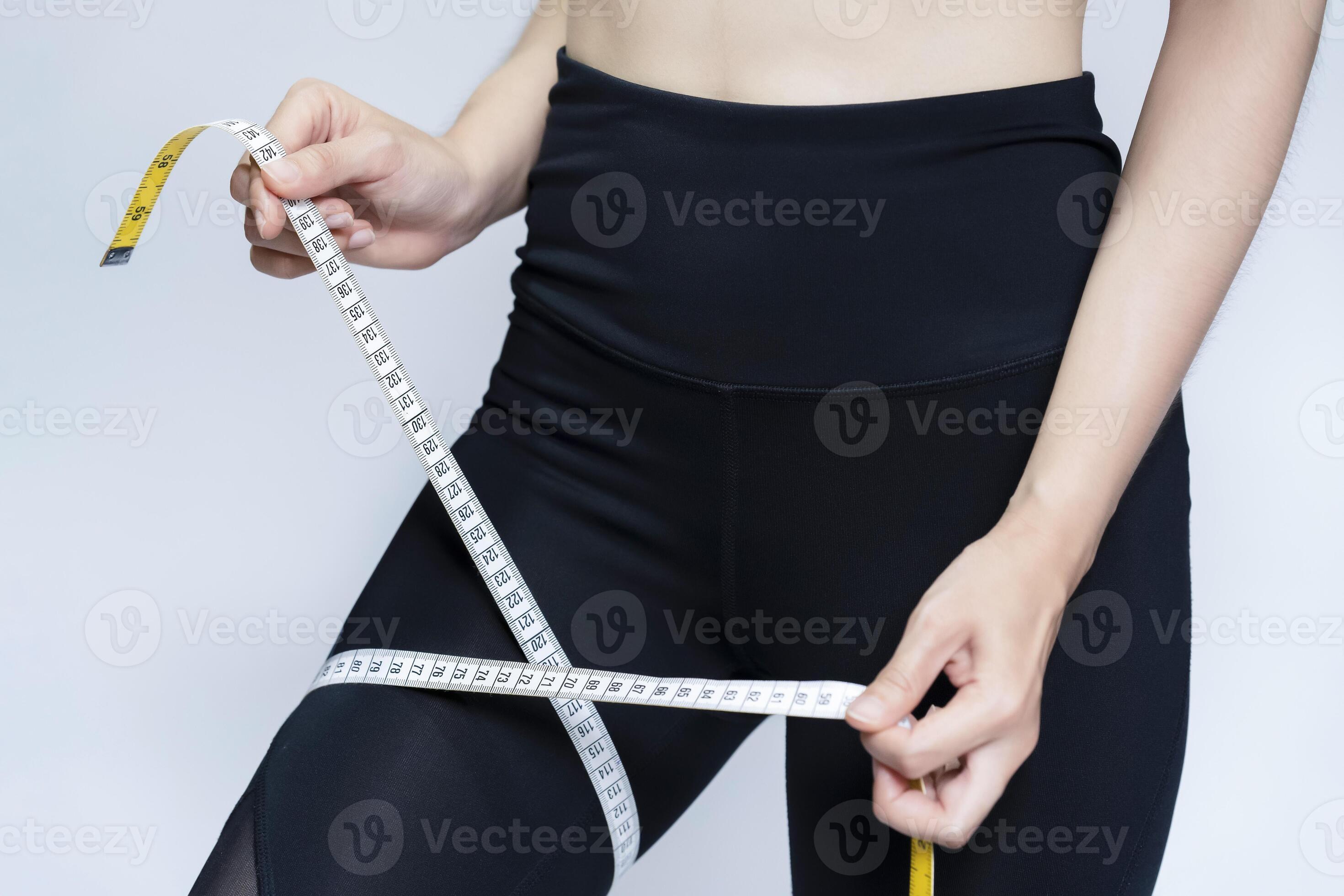 A skinny woman uses a tape measure around her thigh with gray