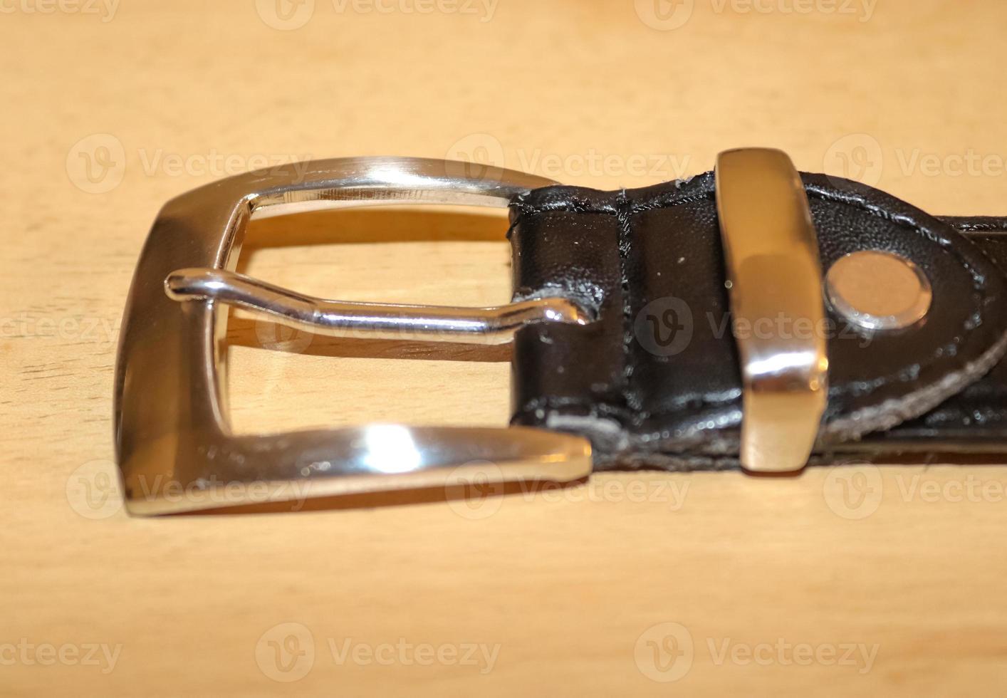 Slightly old black leather belt with a metal buckle on old wooden background photo