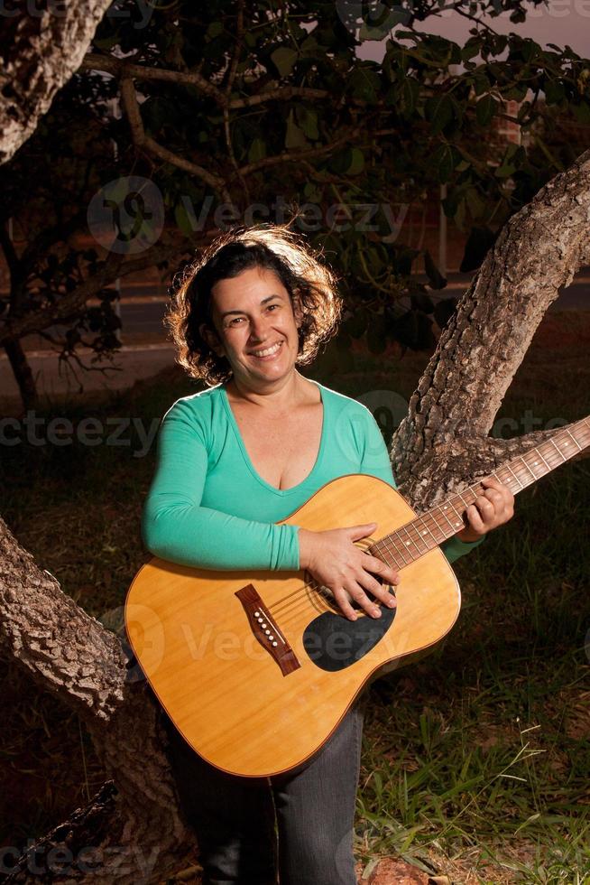 Happy Mature woman playing and singing with her acoustic guitar in the park photo