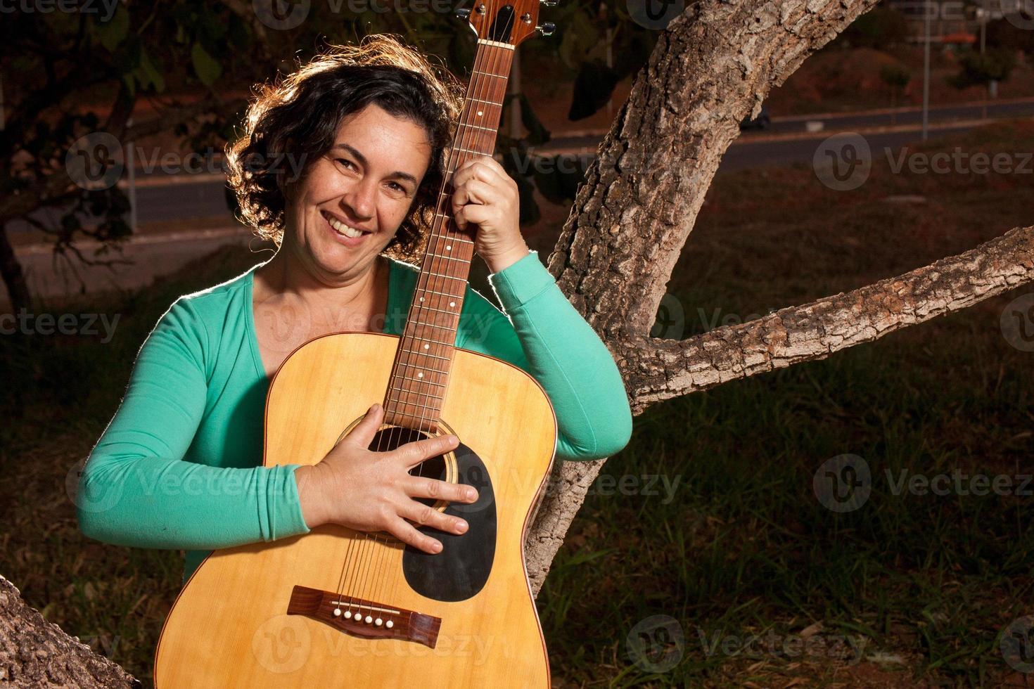 mujer madura feliz tocando y cantando con su guitarra acústica en el parque foto