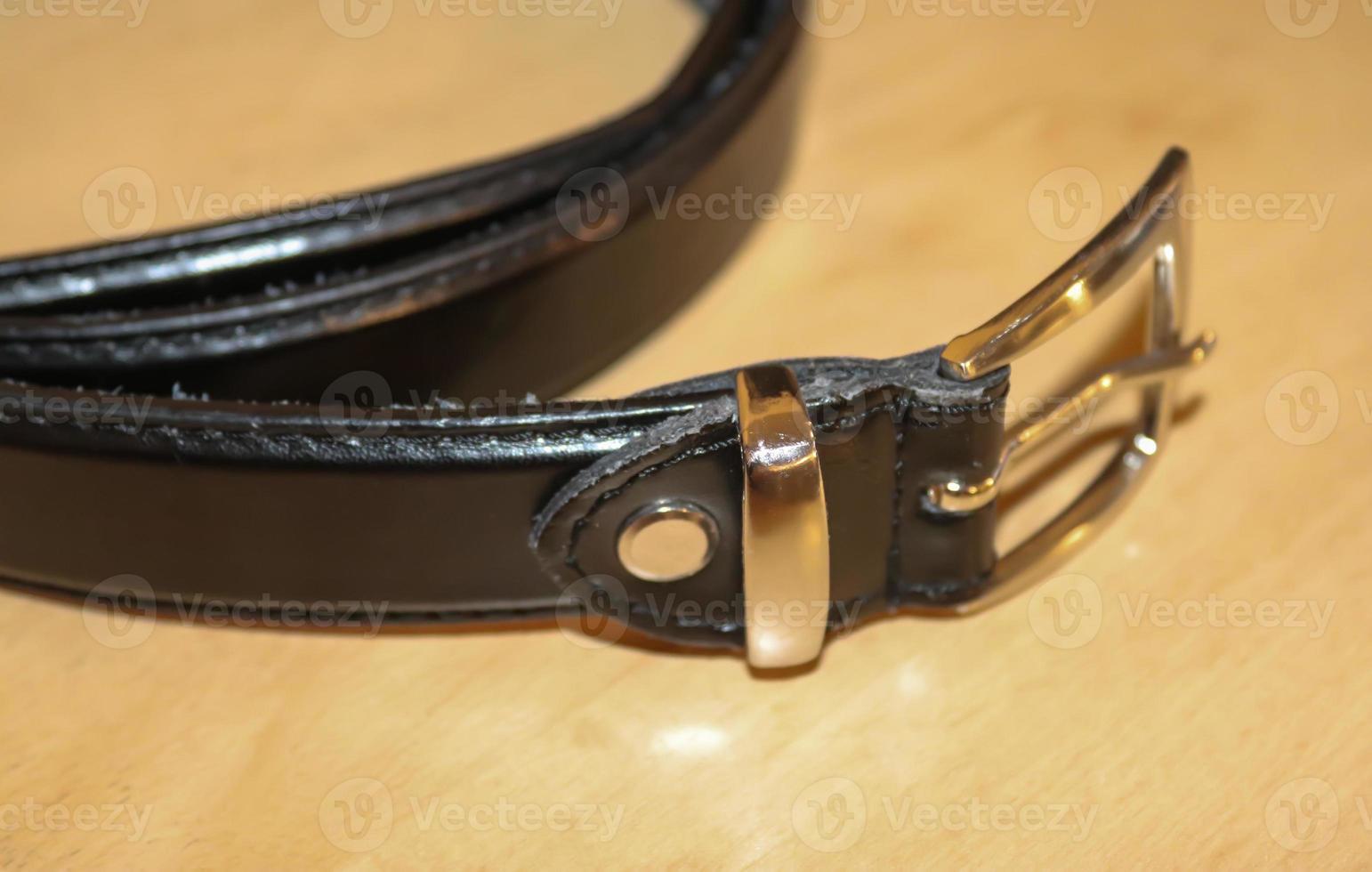 Slightly old black leather belt with a metal buckle on old wooden background photo