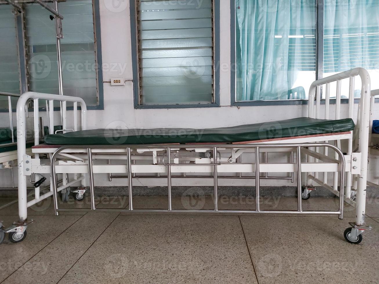 Old hospital bed with green mattress, white steel frame, silver handrails and wheels. photo