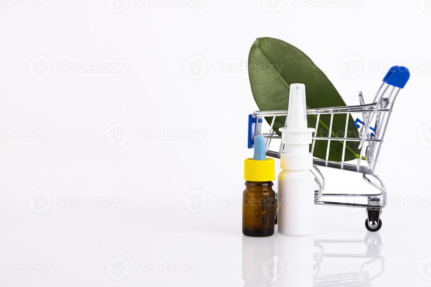 Blank amber glass essential oil bottle with pipette, nasal spray on green leaves background. photo