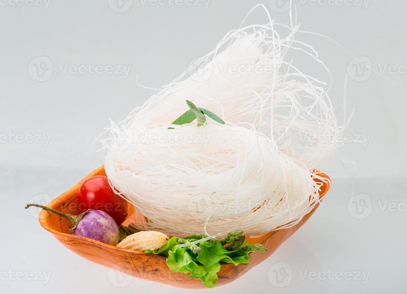 Fideos de arroz crudo en un recipiente sobre fondo blanco. foto