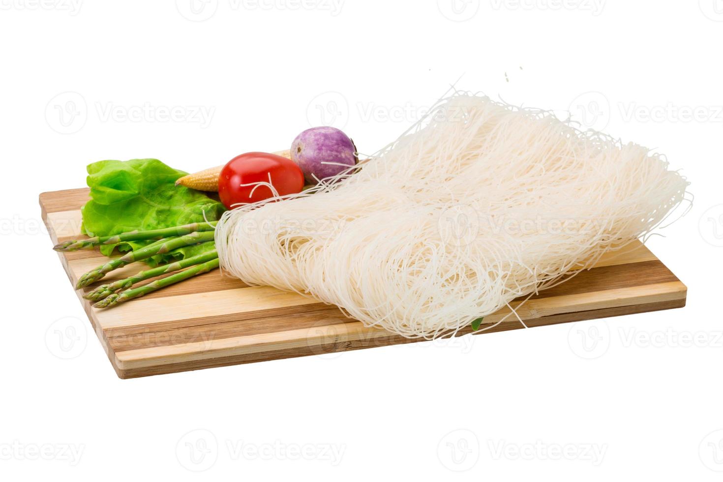 fideos de arroz crudo en plato de madera y fondo blanco foto