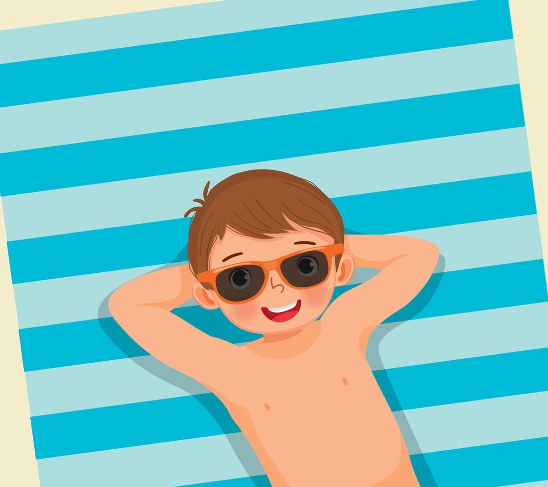 vista superior de un niño lindo con traje de baño y gafas de sol acostado en una toalla de playa divirtiéndose tomando el sol en las vacaciones de verano vector