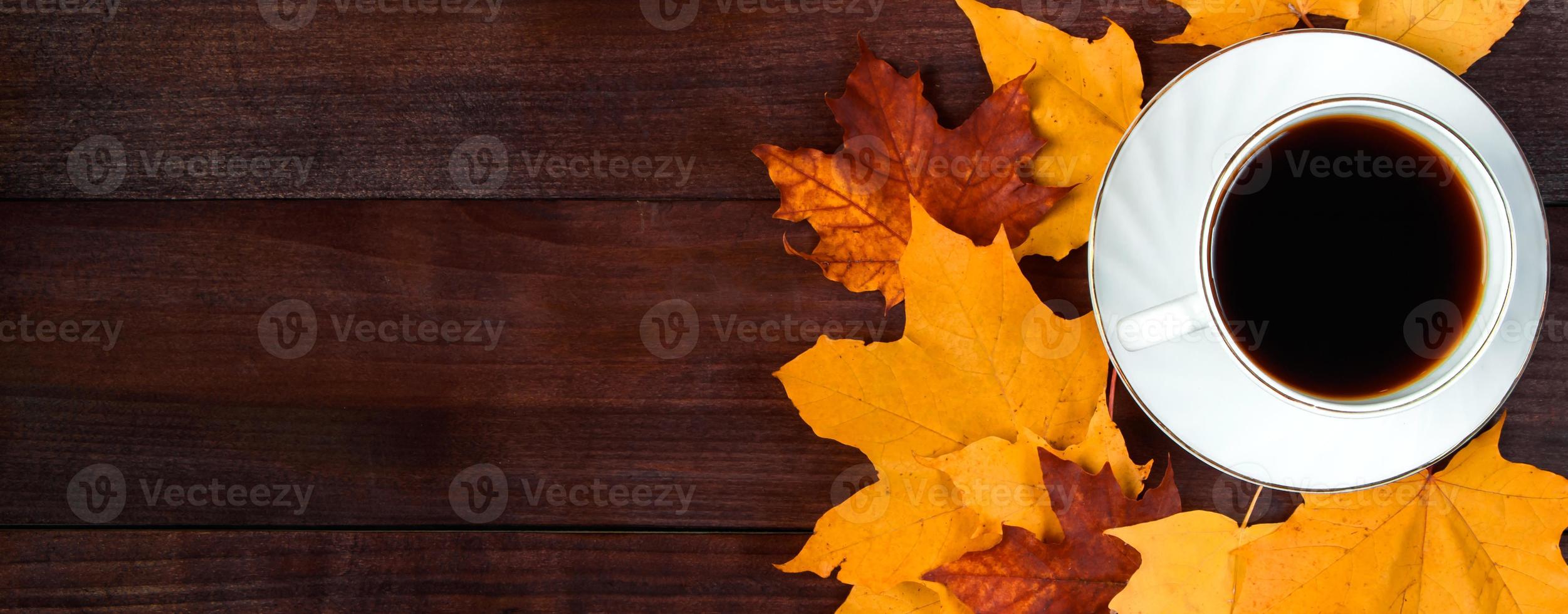 Cup of hot strong coffee and fallen leaves on wooden background. Hello autumn concept. Warm beverage for cold weather. photo