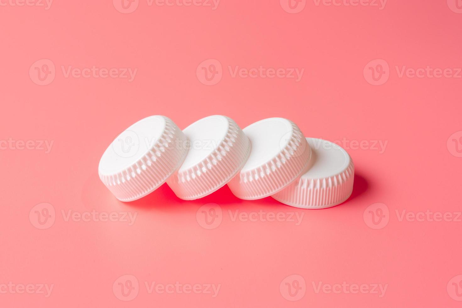 White bottles cap on light pink background. photo