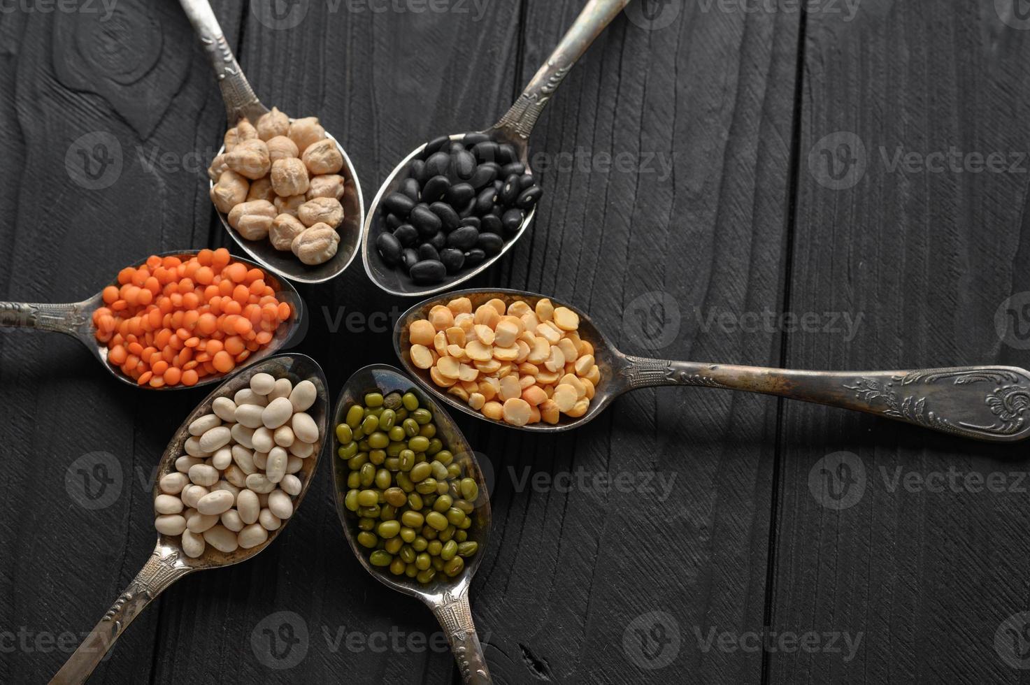 Variety of legumes in old silver spoons on a black wooden background. photo