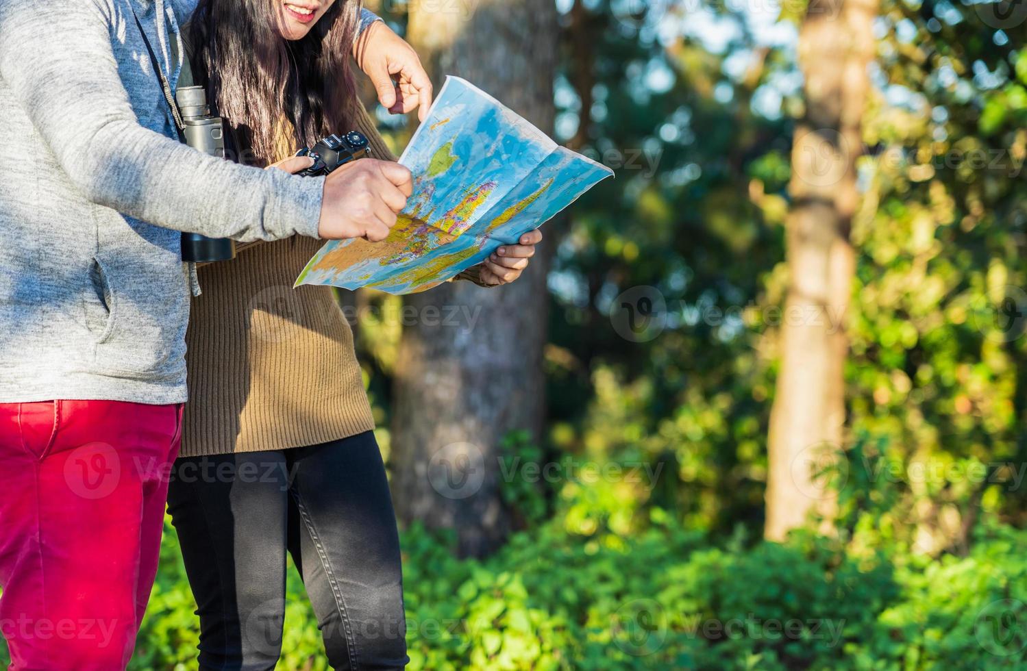 Traveler man and woman are in forest with binoculars and searching location in the map amongtrees big trees. photo