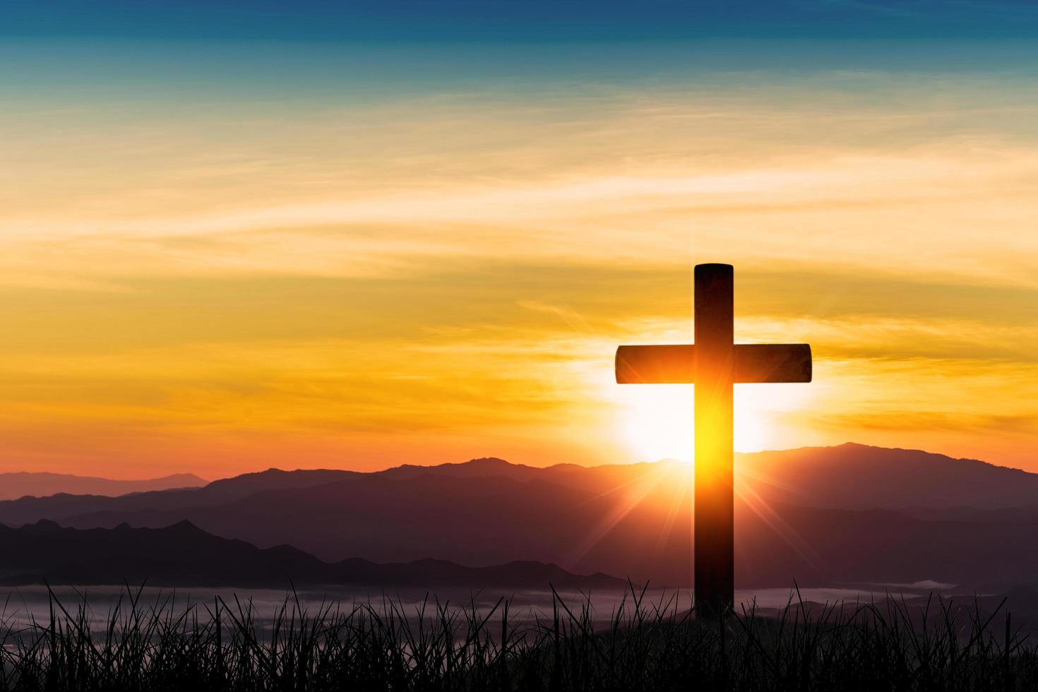 silueta de cruz sobre fondo de puesta de sol de montaña. foto