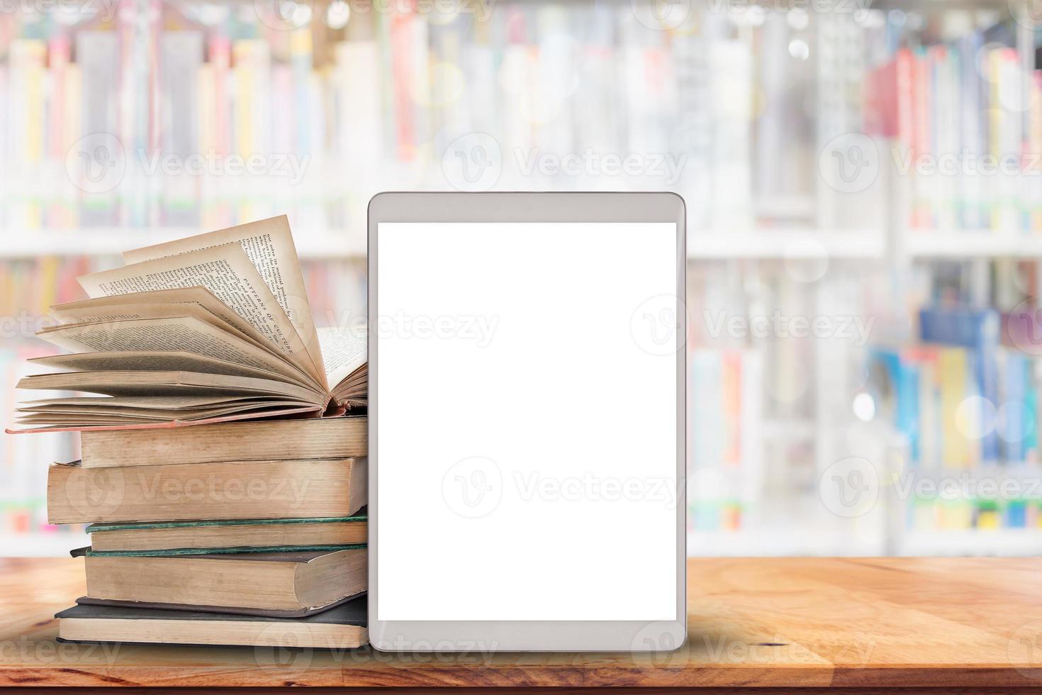 Books and tablet computer on wood table with blurred many books in library background. photo