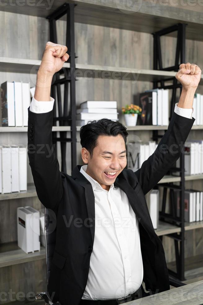 Employee employer employment entrepreneur executive man in formalwear raised hands fists up sit on chair. Emotional guy feeling glad and happy as he's great success, finishes successful business. photo