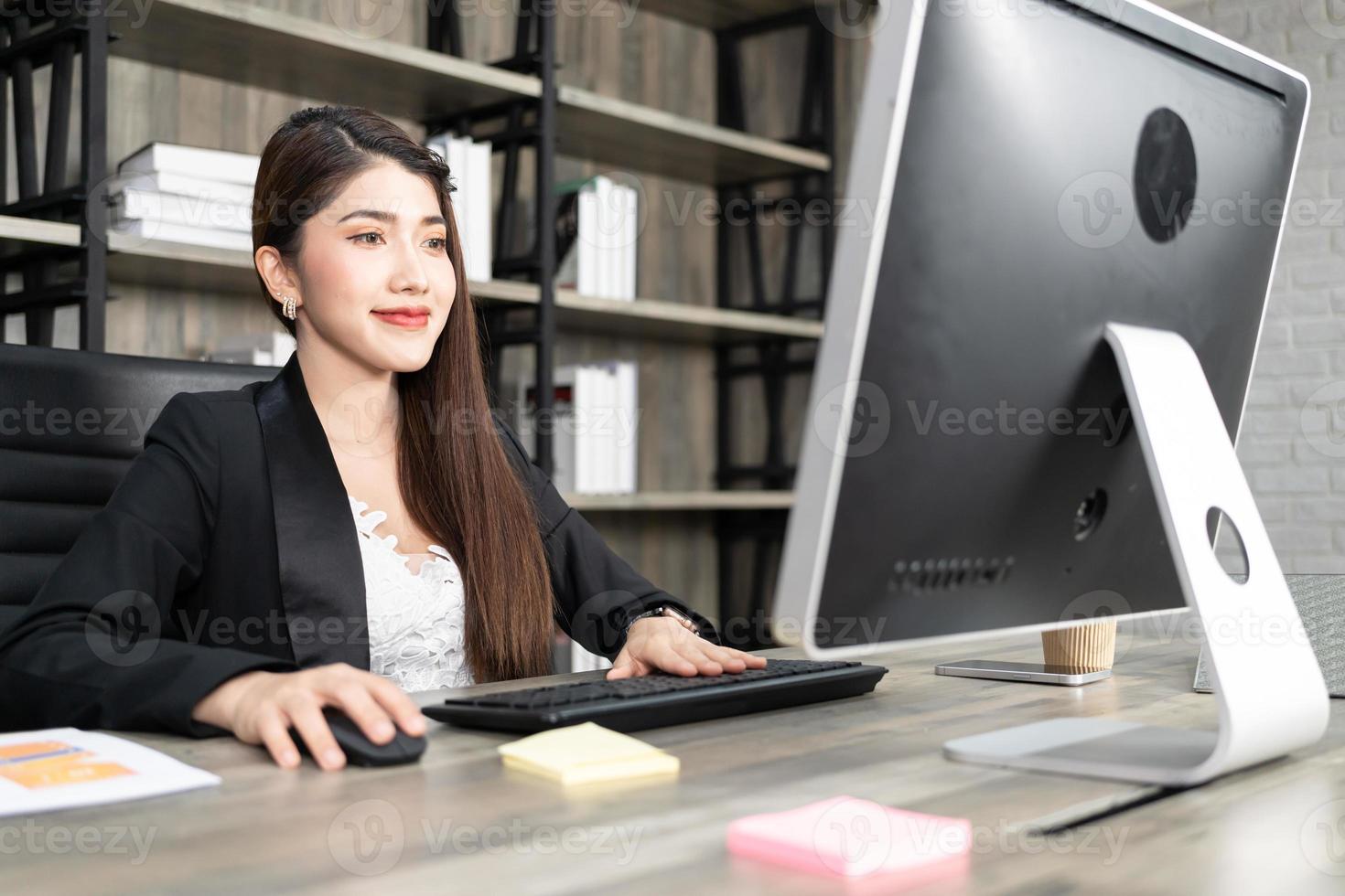 Portrait of pretty business woman using computer at workplace in an office. positive business lady smiling looking into screen of computer. photo