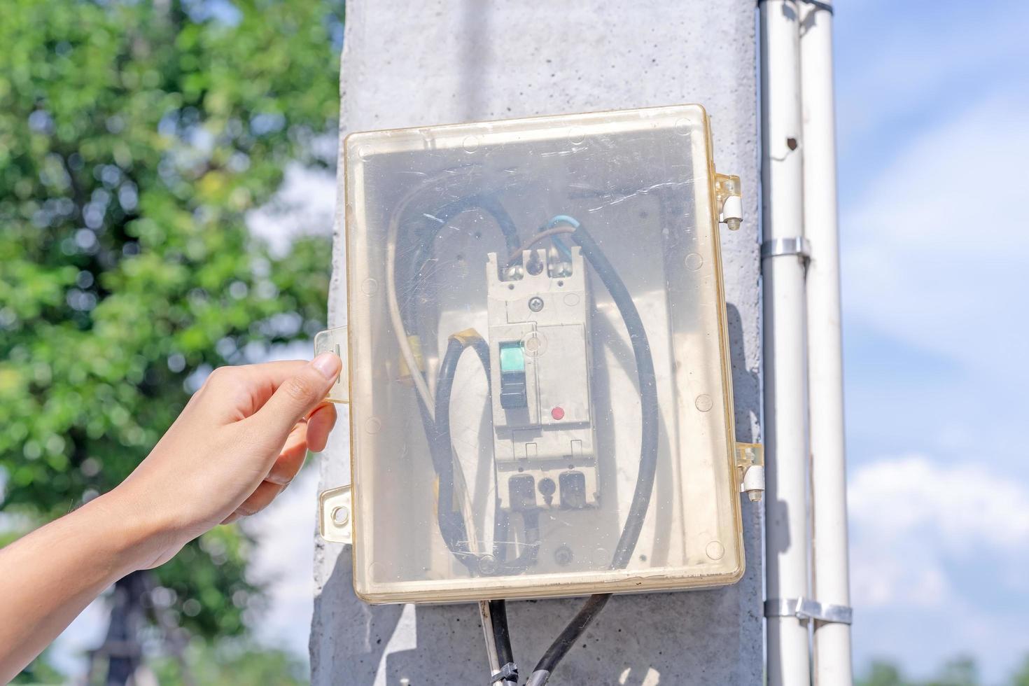 Hand of human electrician opens or closes electrical box on electric pole in park. Switchboard exists between public gardens or streets for convenience of emergency remedies in event of power failure photo