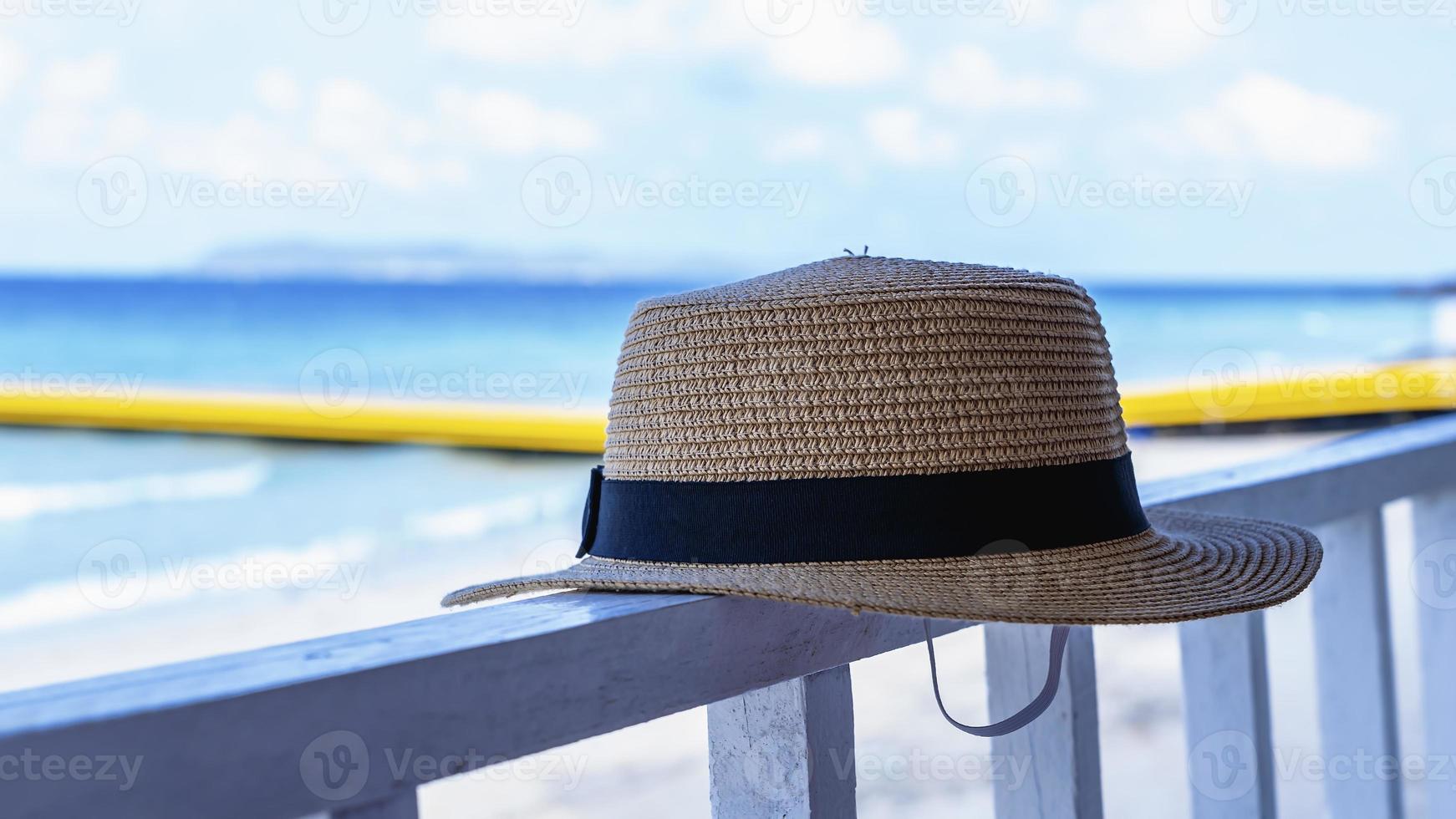 Close-up of straw hat against blurred blue sea background on balcony of the restaurant beside beach. Brown hat of woman relaxing or resting blur background, selective focus. Summer vacation concept photo