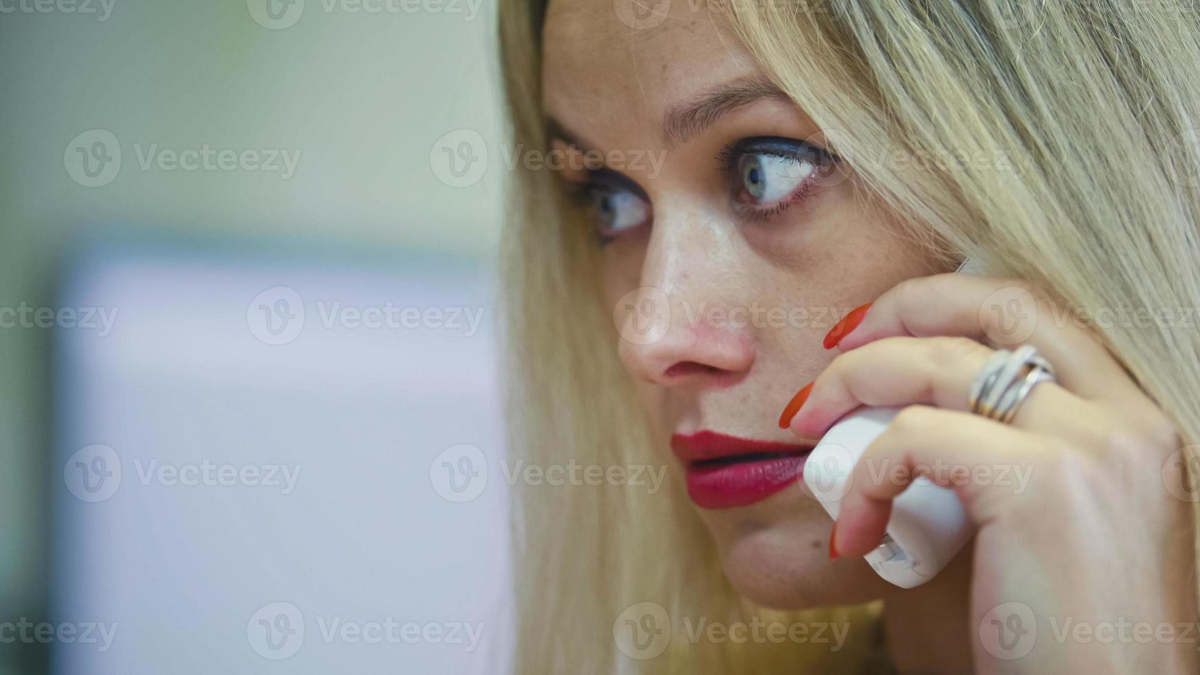 Young Blonde Woman in office talking on phone in front of the computer, extremely close up photo
