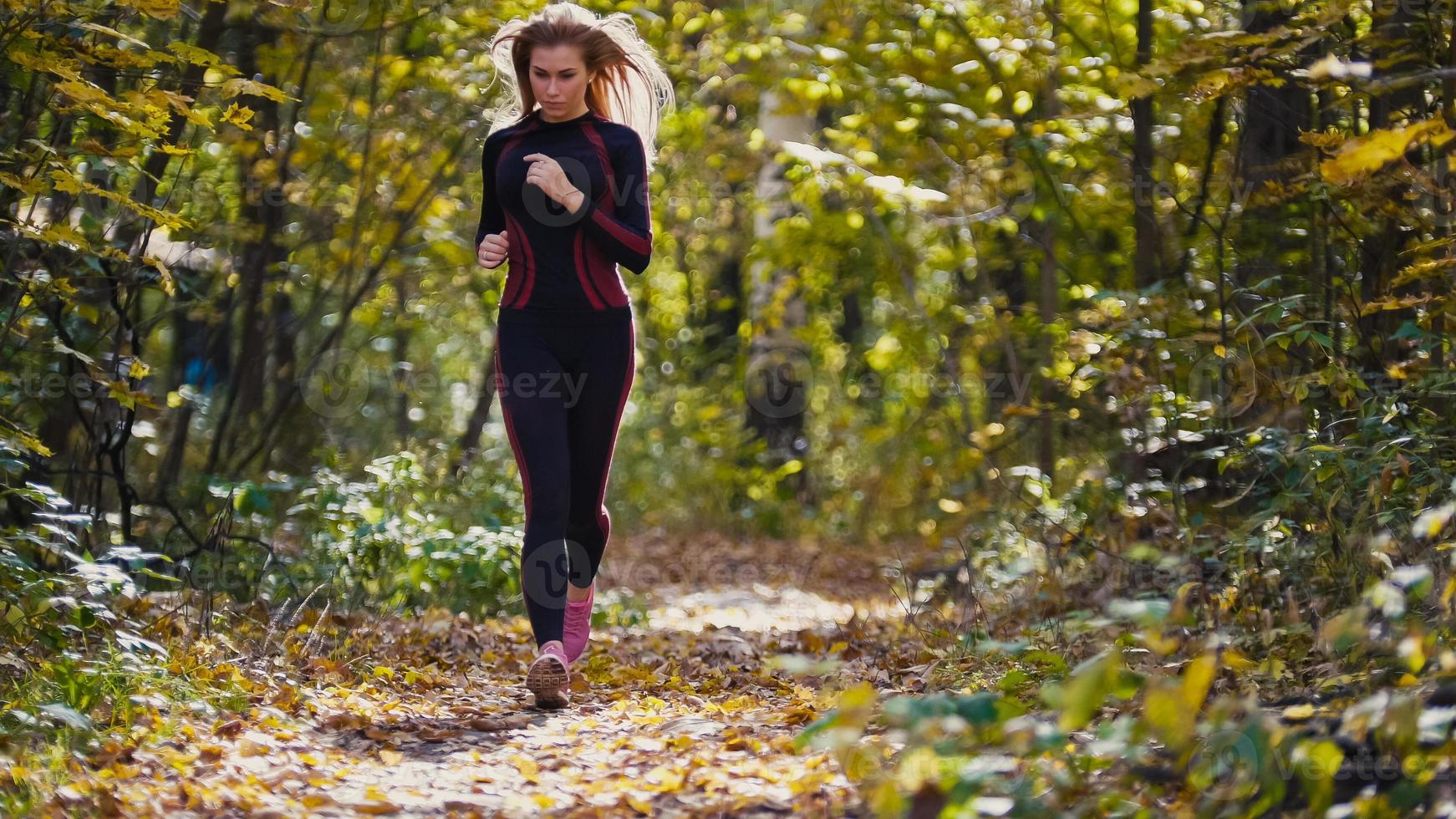 Young runner girl have jogging on autumn road covered with fallen leaves. Sports healthy lifestyle concept photo