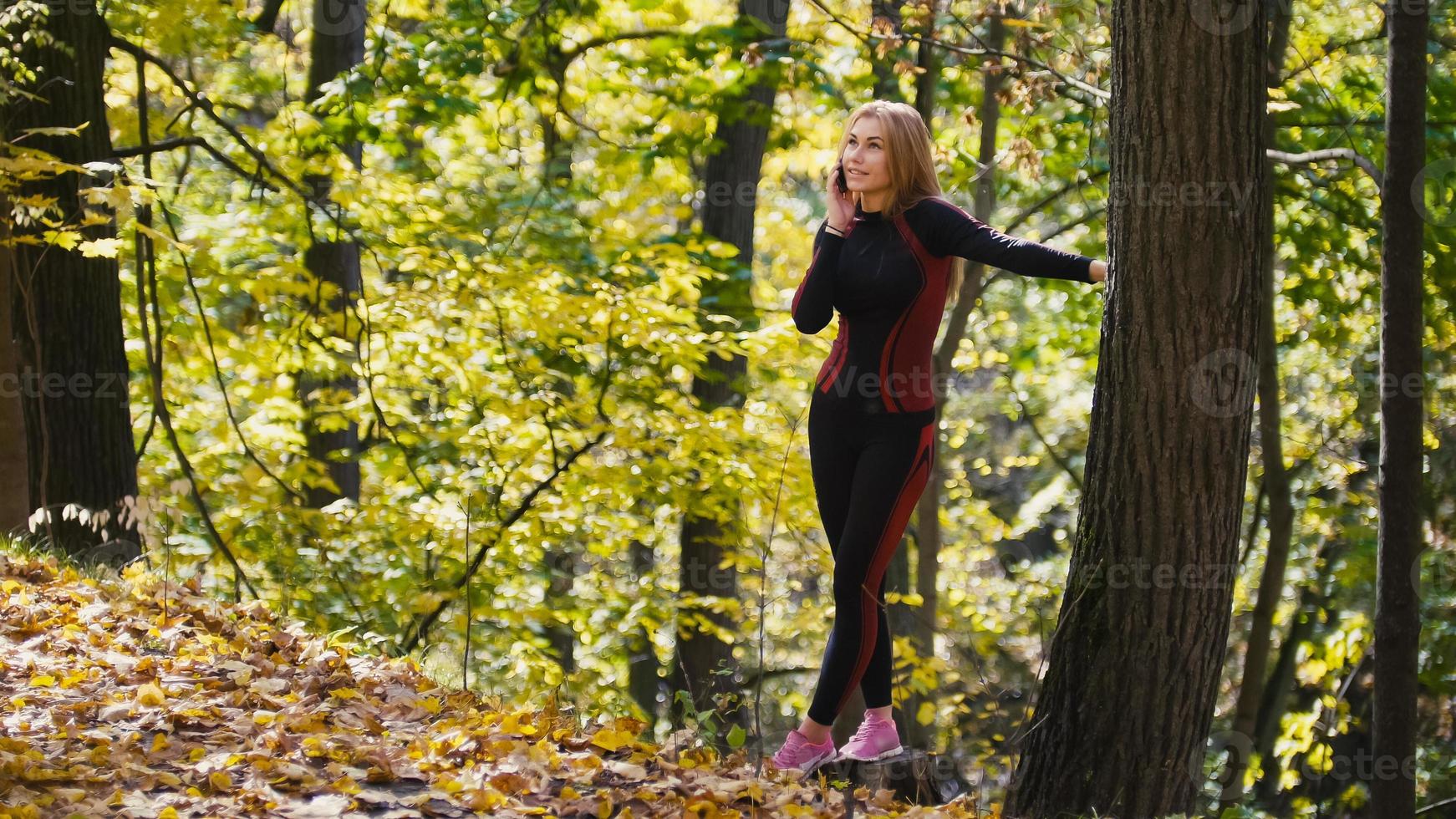 mujer joven y deportiva hablando por celular en el parque de otoño al aire libre, mirando al cielo foto