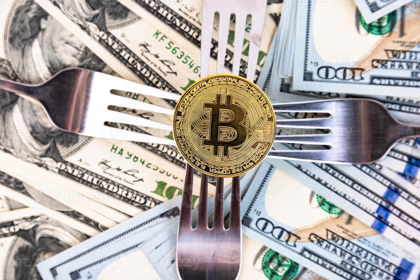 Gold bitcoin on the background of one hundred dollar bills and cutlery. photo