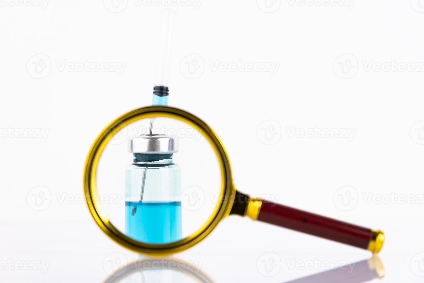 Medical ampoule and syringe through a magnifying glass, on a white background. Vaccination concept for children and adults. Copy space. photo