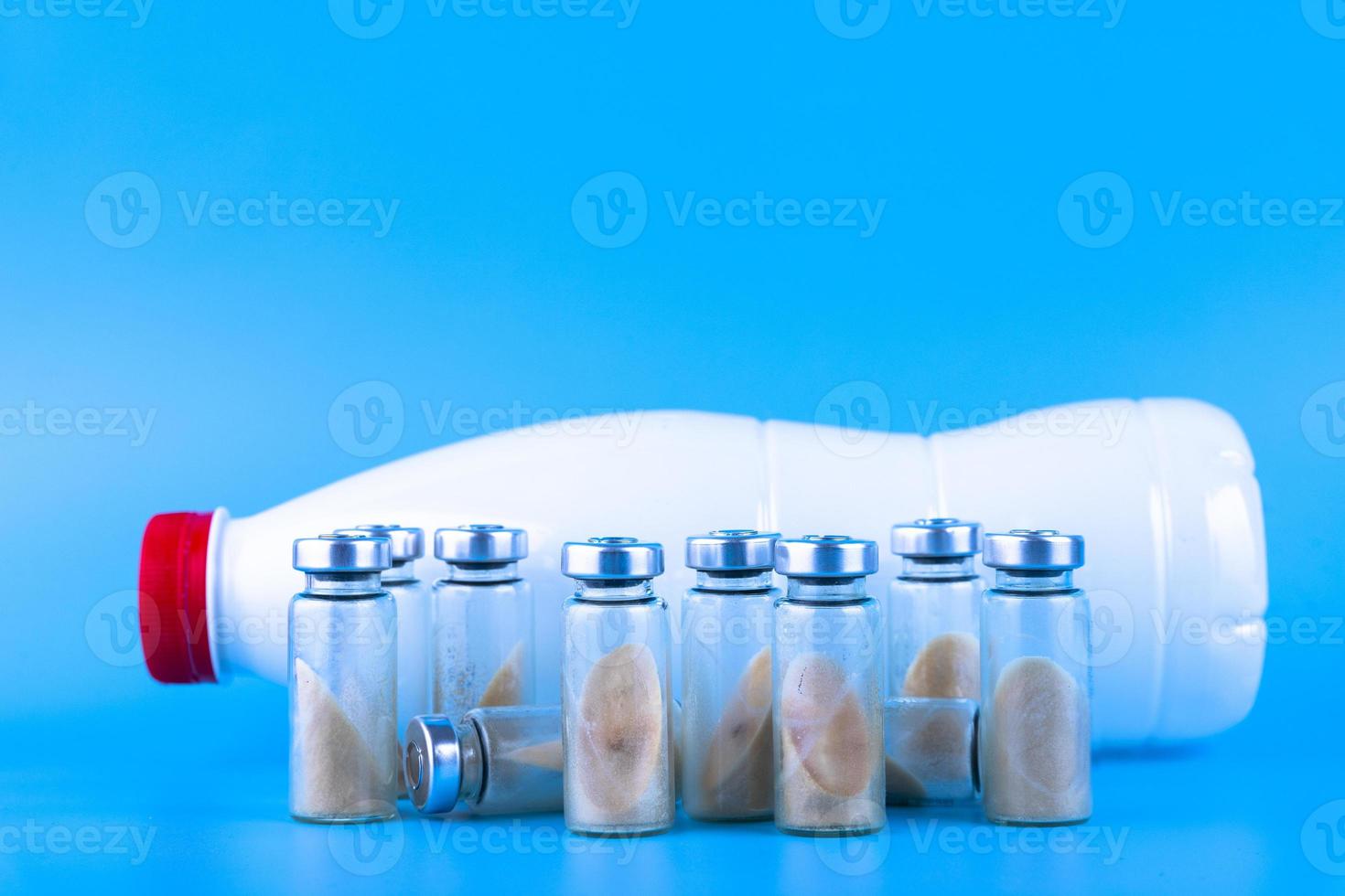 Vials, ampoules with dry probiotic, bifidobacteria and a bottle with milk on a blue background. Copy space. photo