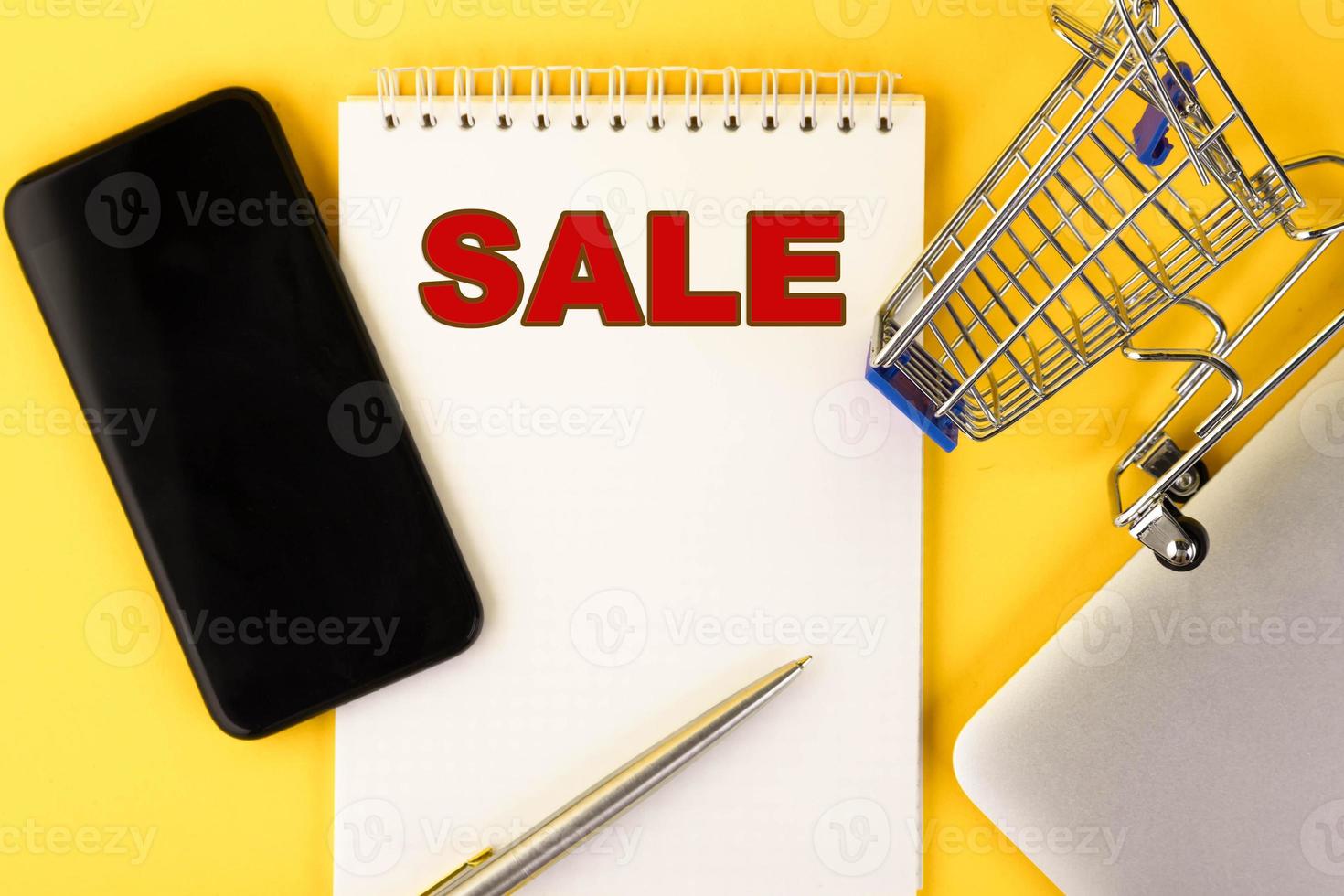 SALE text written in a notebook in red letters lies on the table on a yellow background. Copy space. photo