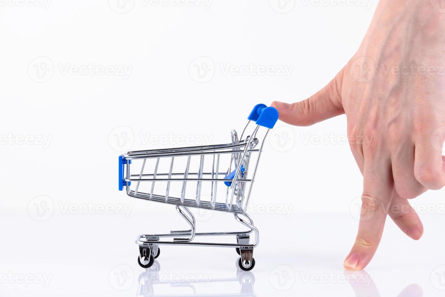 Female hand with fingers in the form of a walking man, pushing a shopping cart, isolated on a white background. Copy space. photo
