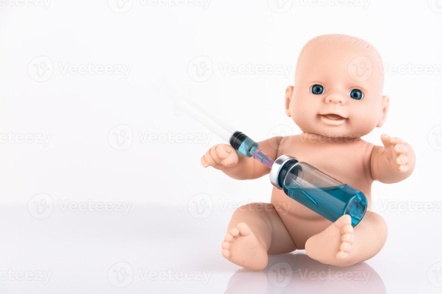 The baby doll is holding a medical syringe and an ampoule with a vaccine. Vaccine for newborns Concept. Copy space. photo