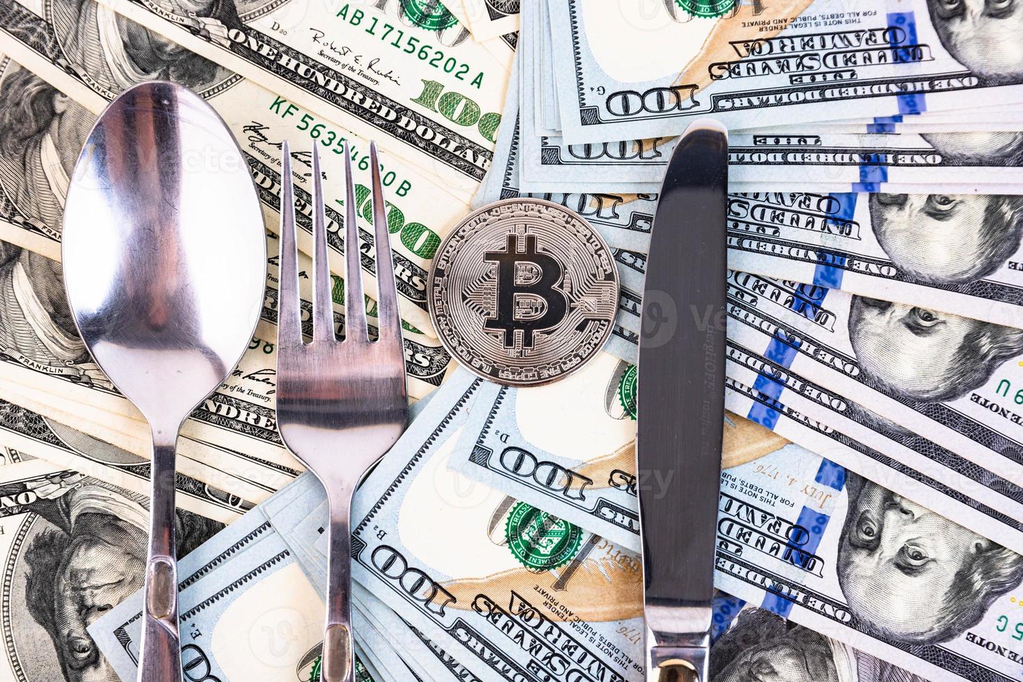 Platinum bitcoin on the background of one hundred dollar bills and cutlery. photo