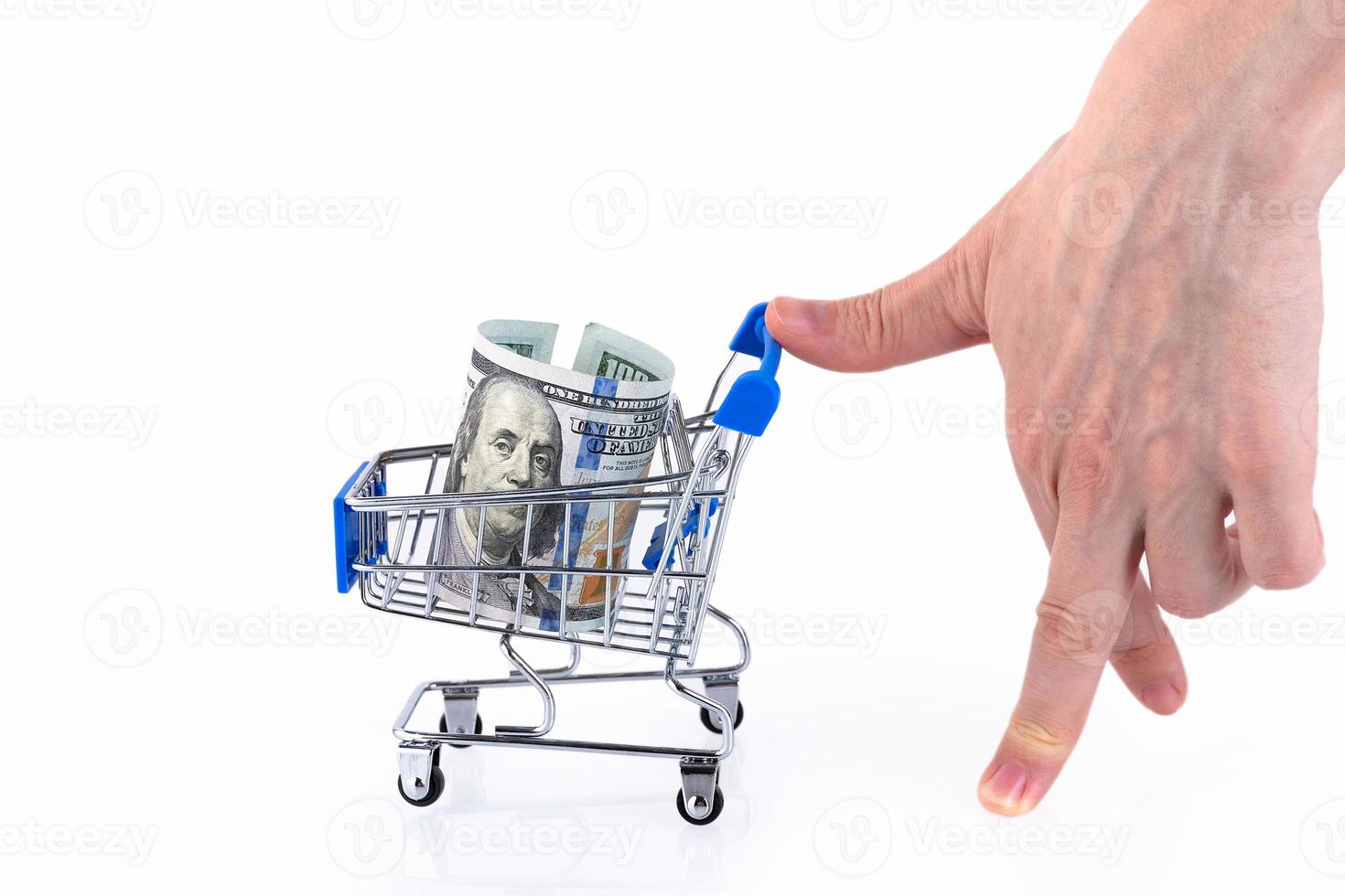 A hand in the form of a walking man rolls up a shopping cart with a roll of one hundred dollar bills. Copy space. photo