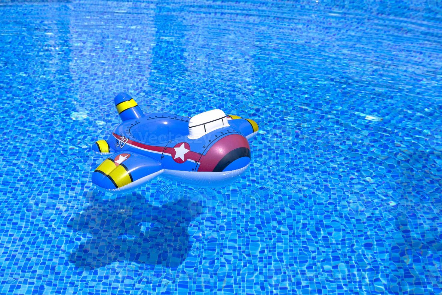 Water ripple on blue tiled pool background. Turquoise water with a floating children's inflatable ring in the form of an airplane. copy space photo