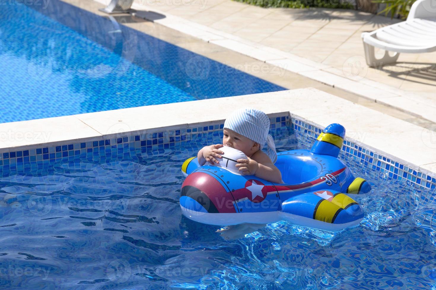 .A child is floating in an inflatable rubber circle in the form of an airplane. A child in an outdoor pool with blue water, photo