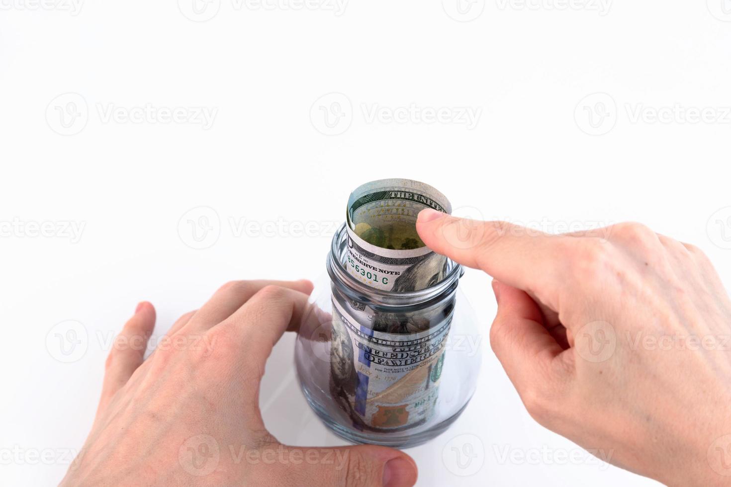 Hand folds paper American one hundred dollar bills, money in a glass jar. Concept for making deposits, saving money. White background. Copy space. photo