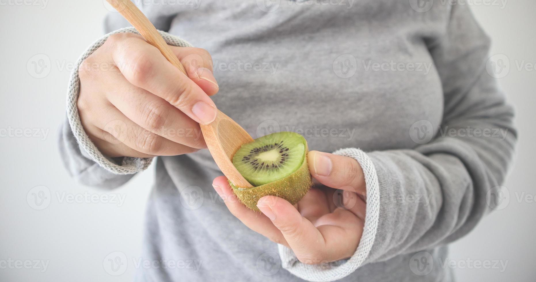 hembra joven comiendo kiwi maduro con cuchara de madera foto