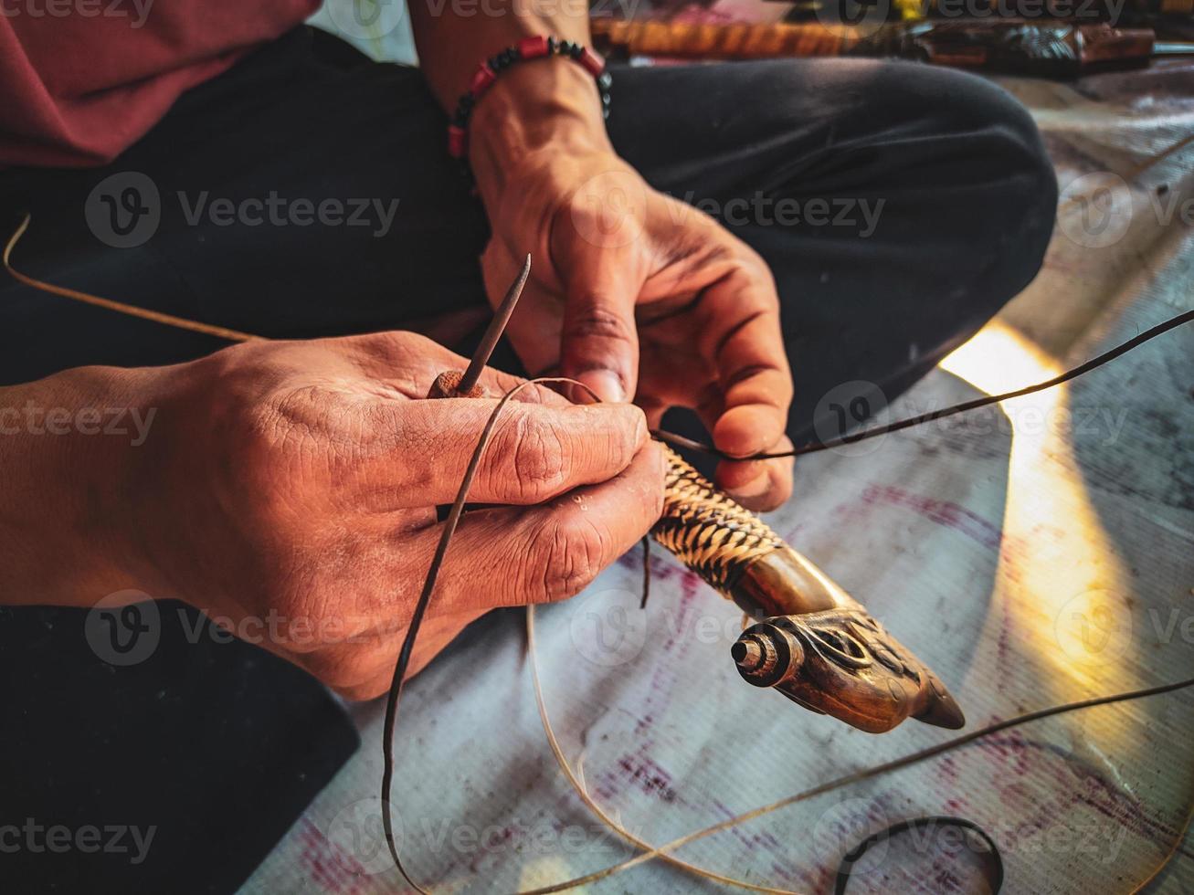close up of a man's hand making a rattan hoop on a mandau handle photo