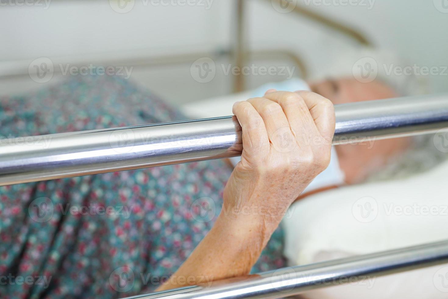 Asian elder senior woman patient holding bed rail while lie down with hope waiting her family in hospital. photo