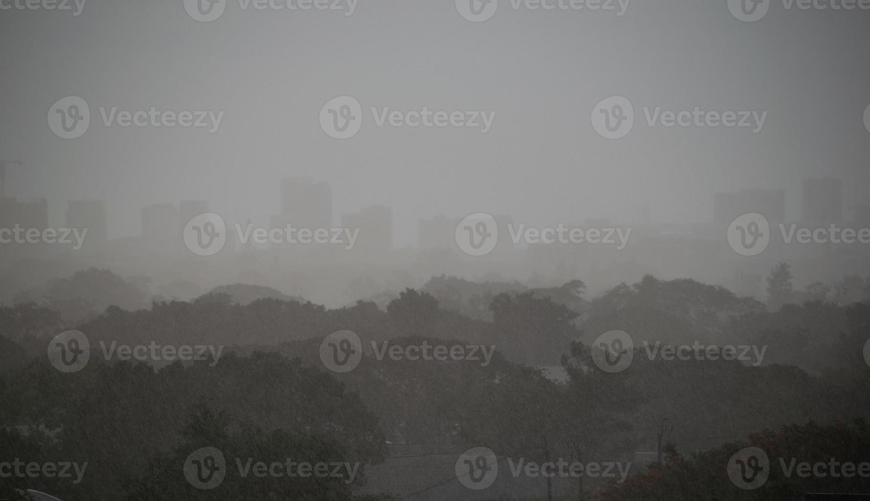 Background heavy rain falling from rainy season sky, tree and building silhouette, tropical Thailand. photo