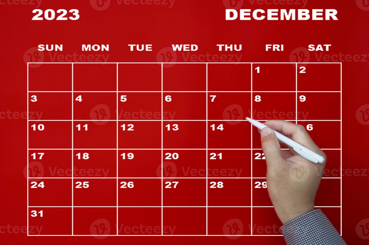 December 2023 calendar with hand holding black pen on red background. photo