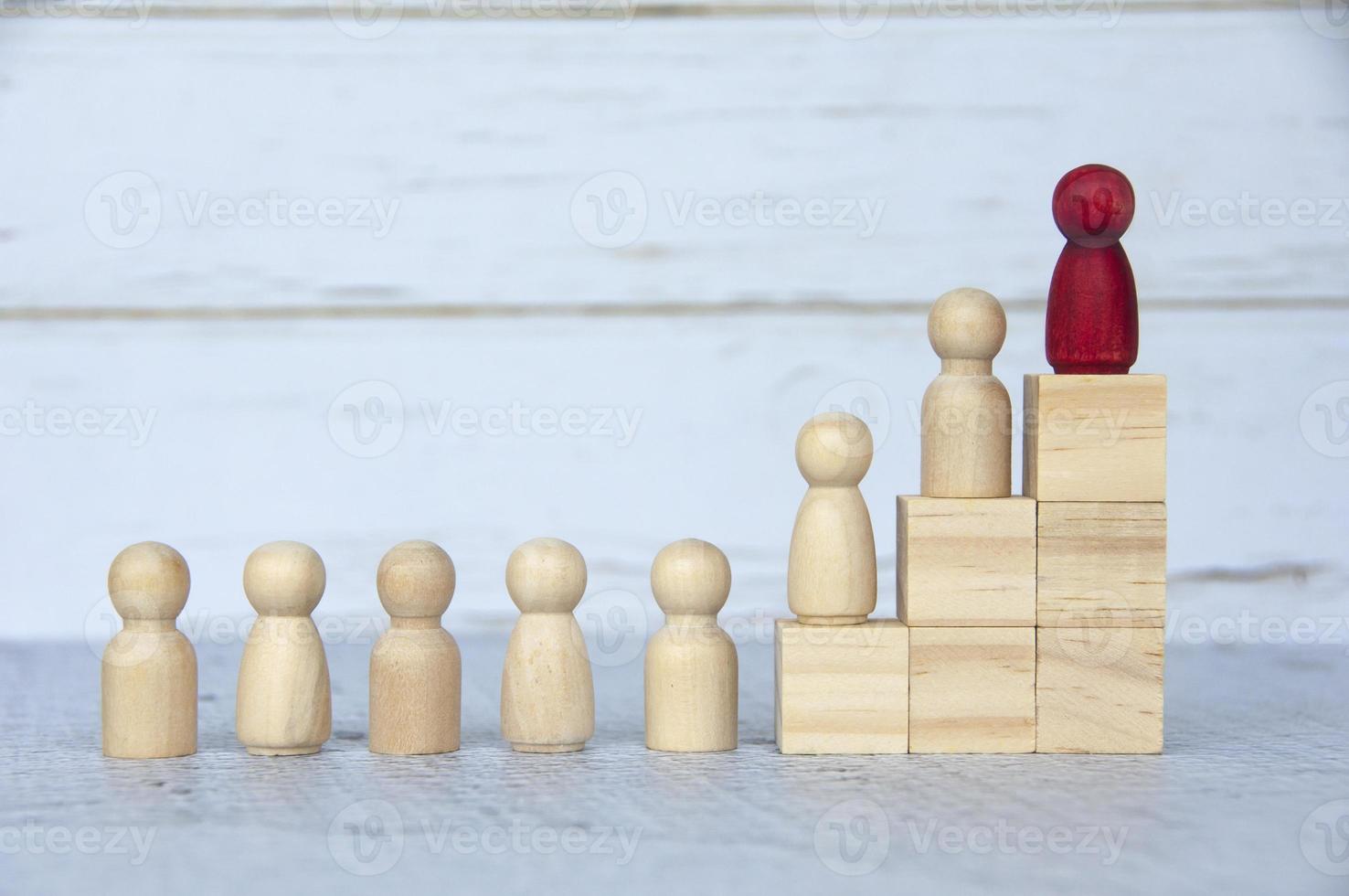 Wooden people figures on top of wooden blocks with red figure leading the rest. Business concept photo